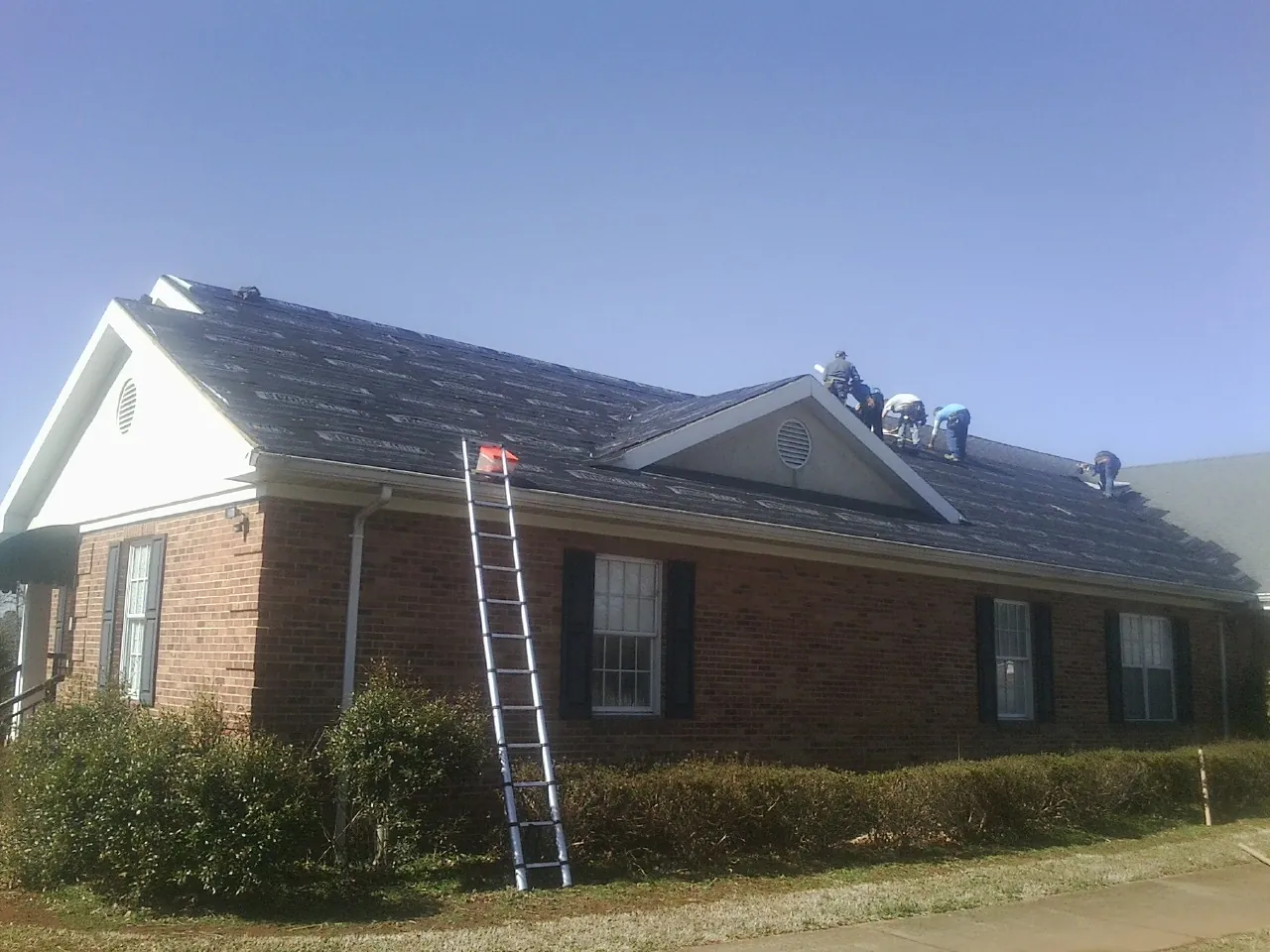 Crew tearing shingles off a brick ranch roof with a ladder set — Metal Roof Repair work by our crew in Bristol